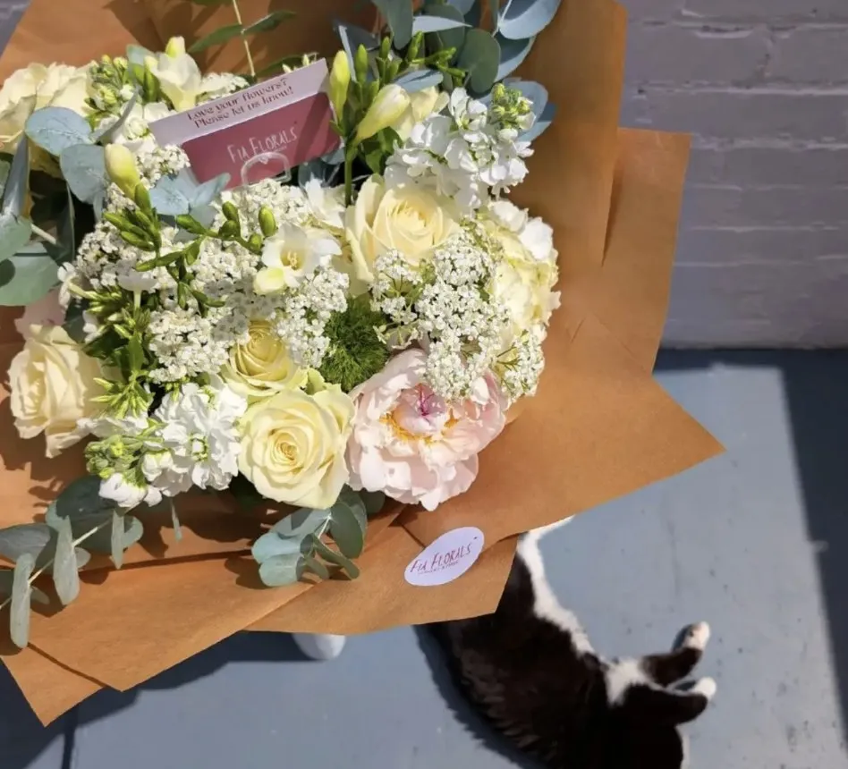Hardy the black and white cat stretched out beside a bouquet