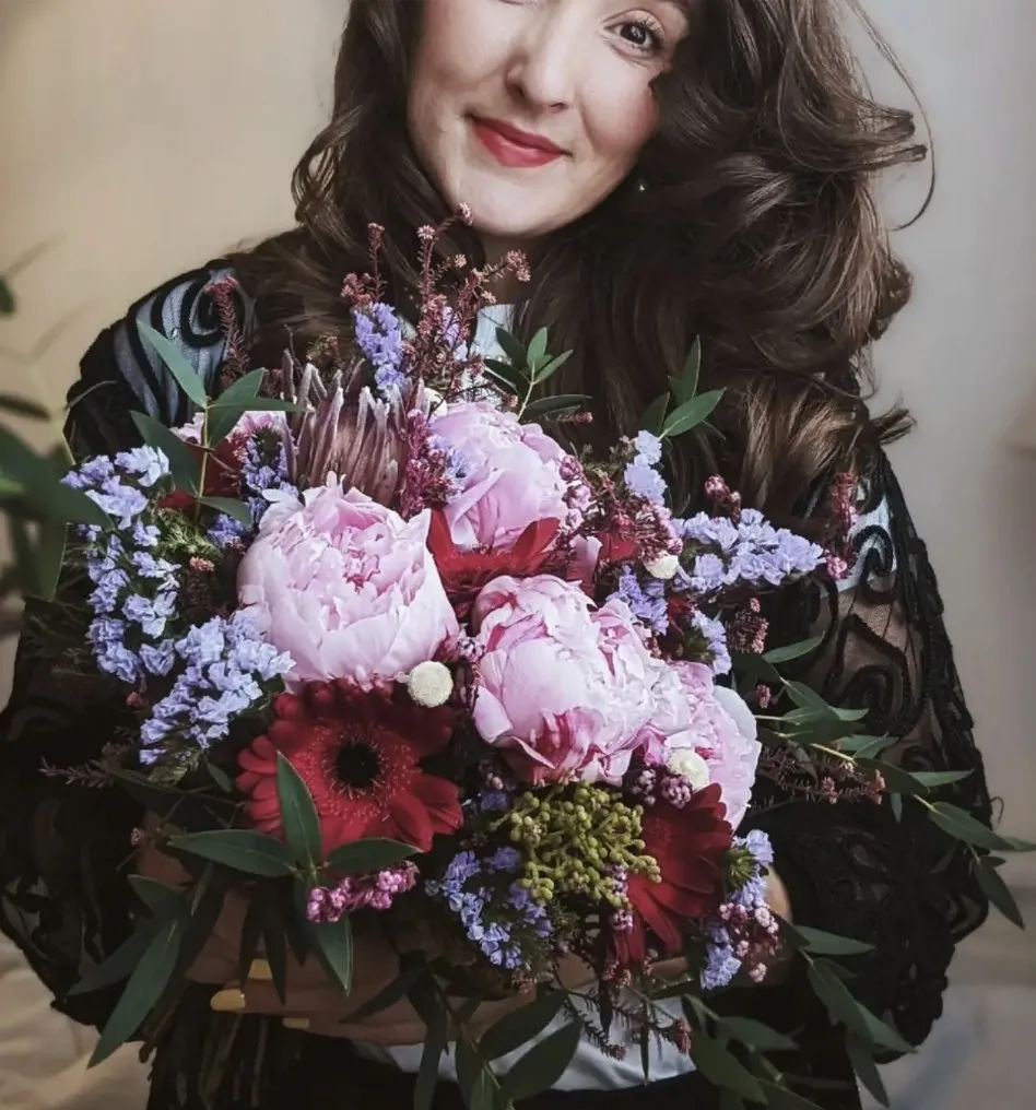 Sophia, owner of Fia Florals, smiling over a peony bouquet
